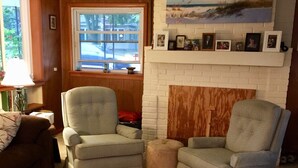 A living room with two armchairs, a small ottoman, a fireplace, and a dog. - House steps from the beach. (Pentwater)
