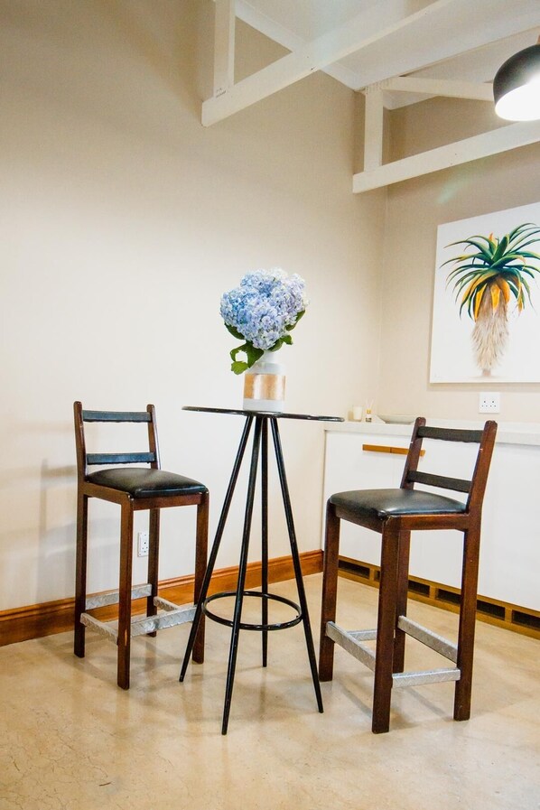 A small, modern room with a round table and two chairs, a vase with blue flowers, and a painting of a plant on the wall.