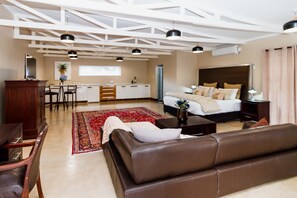 A modern hotel room with a large bed, a sofa, a dining area, and a kitchen.