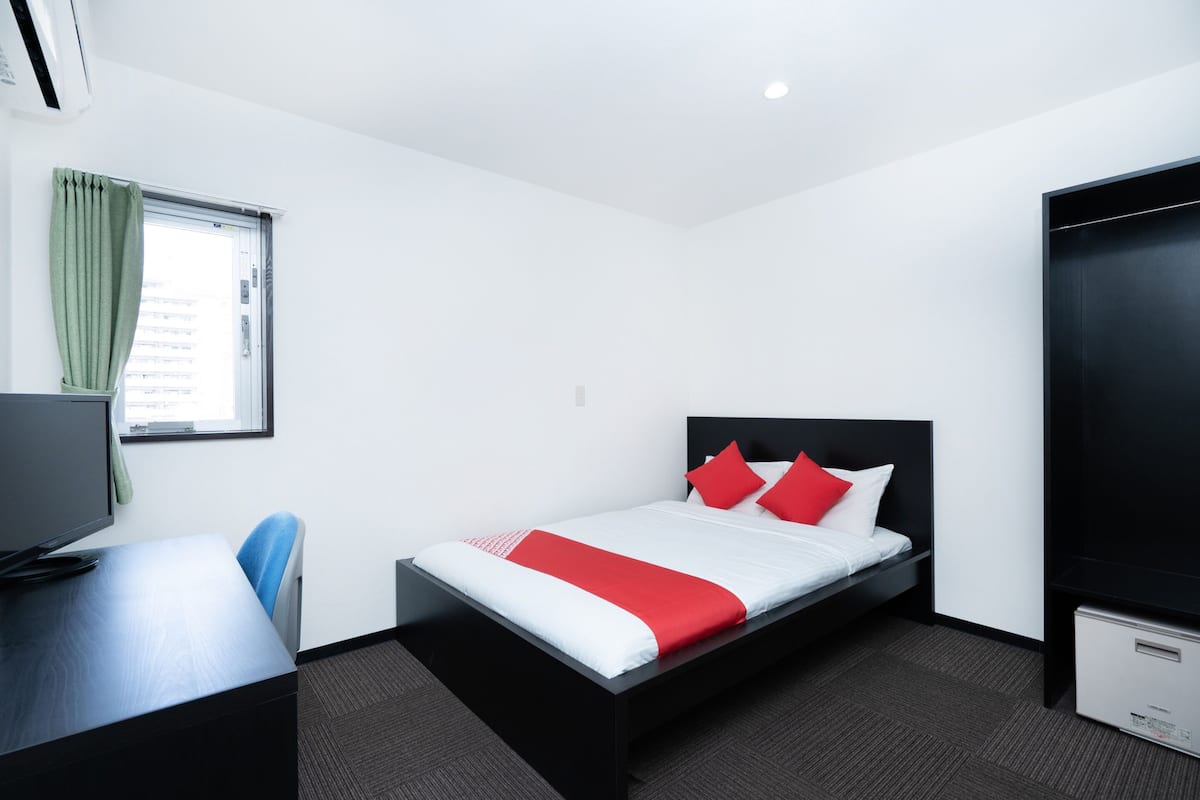 Habitación de hotel con cama, escritorio, televisor y ventana con cortinas.