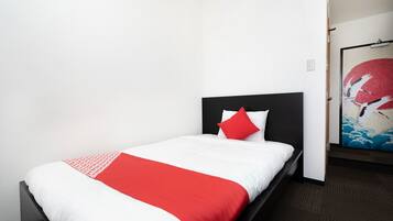 Quarto de hotel com uma cama de solteiro, edredom vermelho e branco e um quadro na parede.