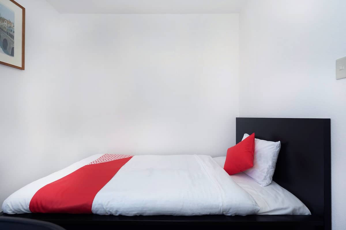 Una cama bien hecha con una colcha blanca y roja, un cabecero negro y una única almohada roja.