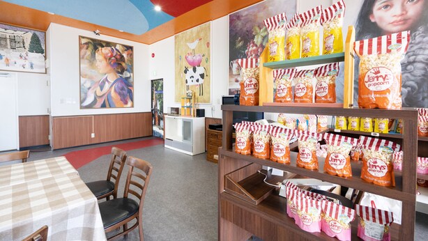 Een restaurant interieur met een geruit tafellaken, houten stoelen en een display met popcorn.