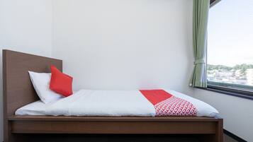 Una cama individual con cabecera de madera, ropa de cama blanca, almohada roja y manta estampada.