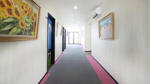 Een gang met kunstwerken in lijsten aan de wanden, een vloerkleed en een airconditioning.