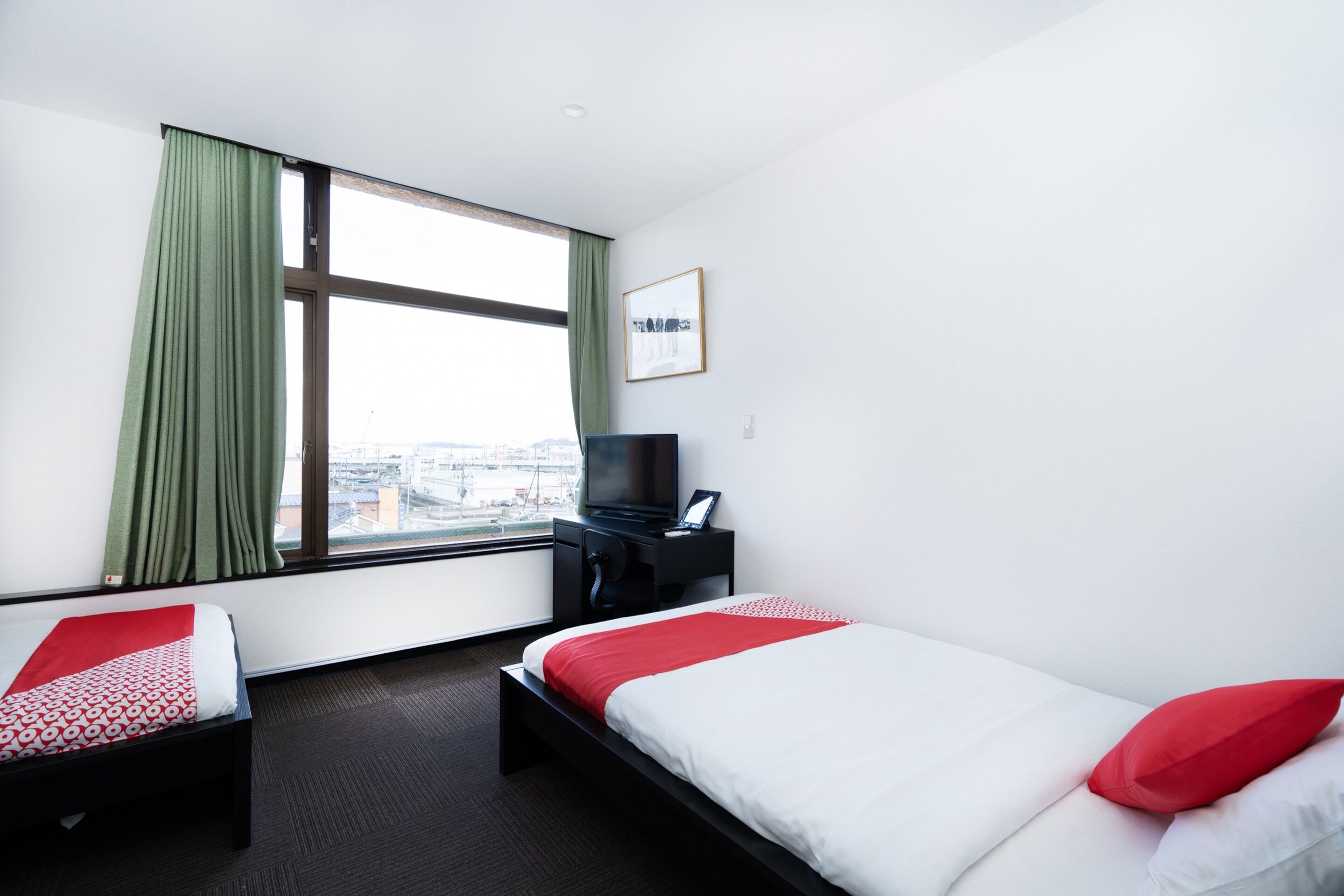 A hotel room with two beds, a TV, a desk, and a window with curtains.