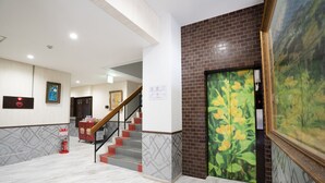 Een hotellobby met een marmeren vloer, een trap, een brandblusser en een schilderij aan de muur.