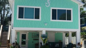 Une maison à deux étages, avec une façade verte, deux grandes fenêtres et un porche couvert doté de sièges pour l’extérieur.