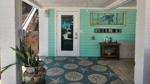 Un couloir avec un mur de couleur turquoise, une porte en bois, un ventilateur de plafond et un tapis à motifs.