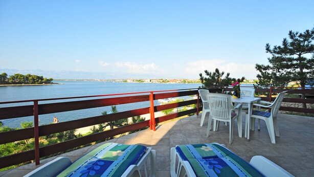 A terrace with a view of the sea, a wooden railing, and two lounge chairs with a table and chairs. - Apartment house by the sea (Nin)