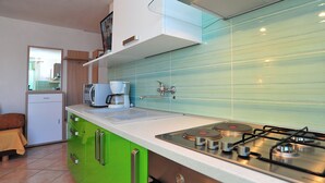 A modern kitchen with green cabinets, a white countertop, a gas stove, and a microwave. - Apartment house by the sea (Nin)