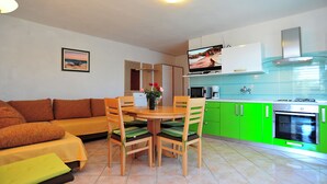 A modern living room with a sofa, dining table, chairs, and a kitchen area with green cabinets and a stove. - Apartment house by the sea (Nin)