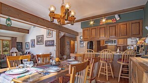 Ein rustikaler Essbereich mit Holztischen und -stühlen, einer Kristallleuchter und einer Küchenzeile mit Holzschränken und einer Bar.