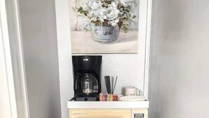 Eine kompakte Küche mit einer Mikrowelle und einer Kaffeemaschine auf einer Arbeitsplatte, darunter ein Kühlschrank und darüber ein gerahmtes Blumenbild.