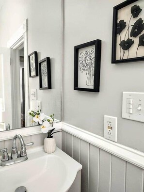 A bathroom with a white sink, a mirror, and framed artwork on the wall.