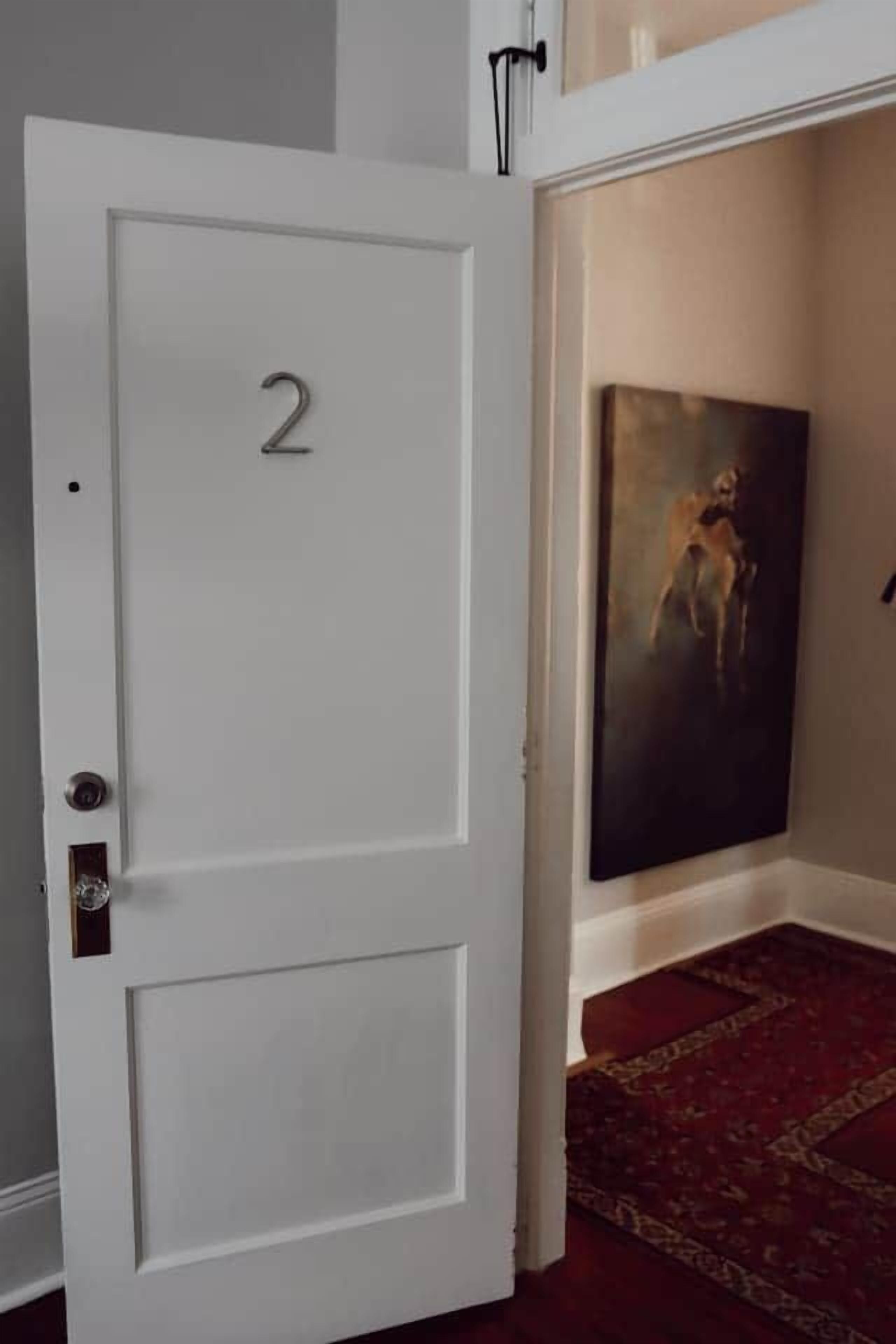 Une porte blanche portant le numéro 2, un tableau accroché au mur et un tapis à motifs.