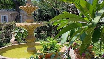 Uma fonte de pedra escalonada, rodeada por vegetação exuberante e plantas em vasos.
