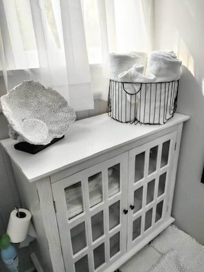A white cabinet with glass doors, a white towel basket, and a white towel on top.