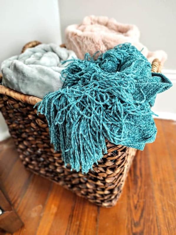 A wicker basket with a teal knitted item and two soft blankets.