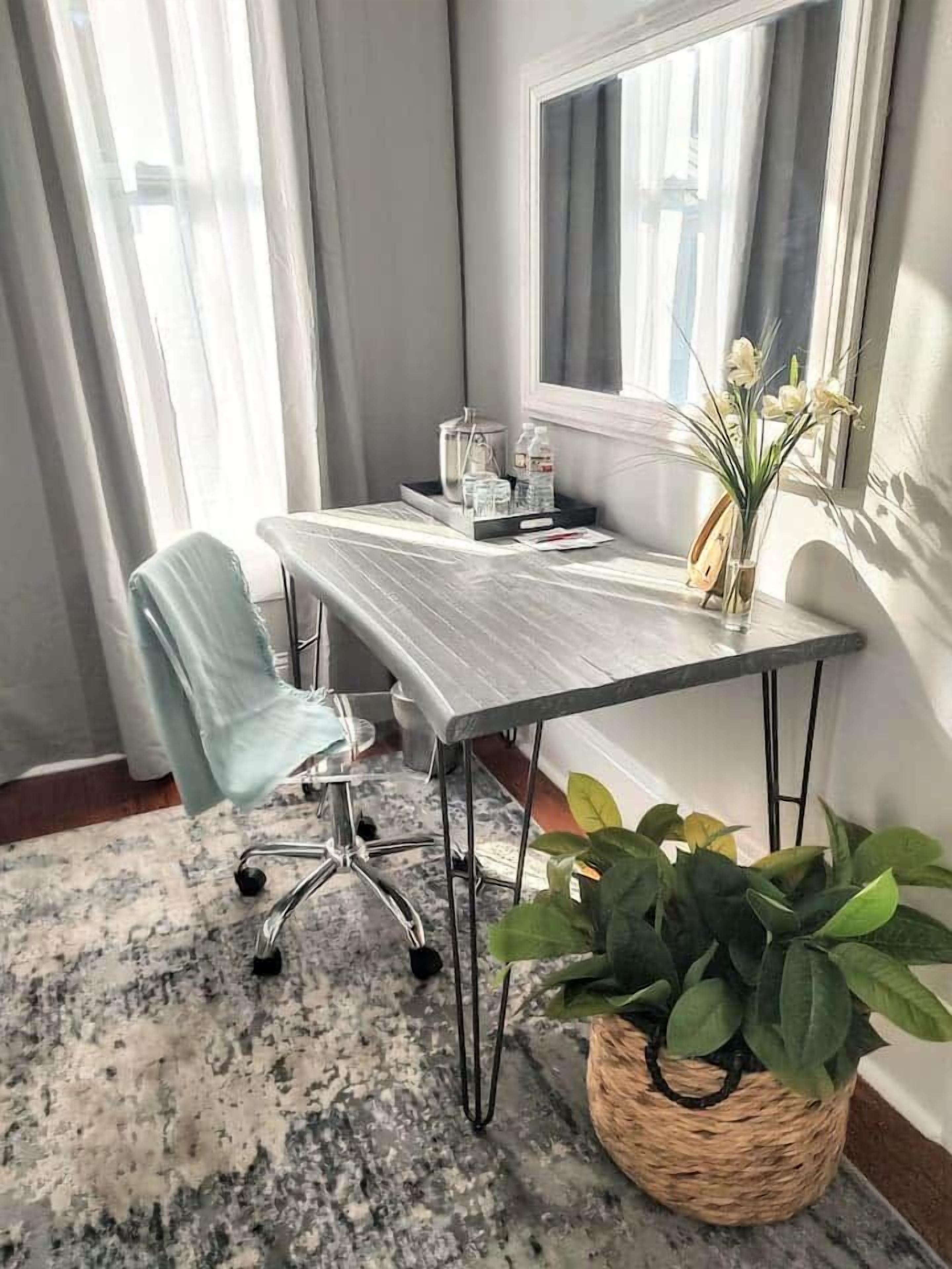 Un espacio de oficina moderno con una mesa larga, una silla, una planta en maceta y un ventanal con cortinas.