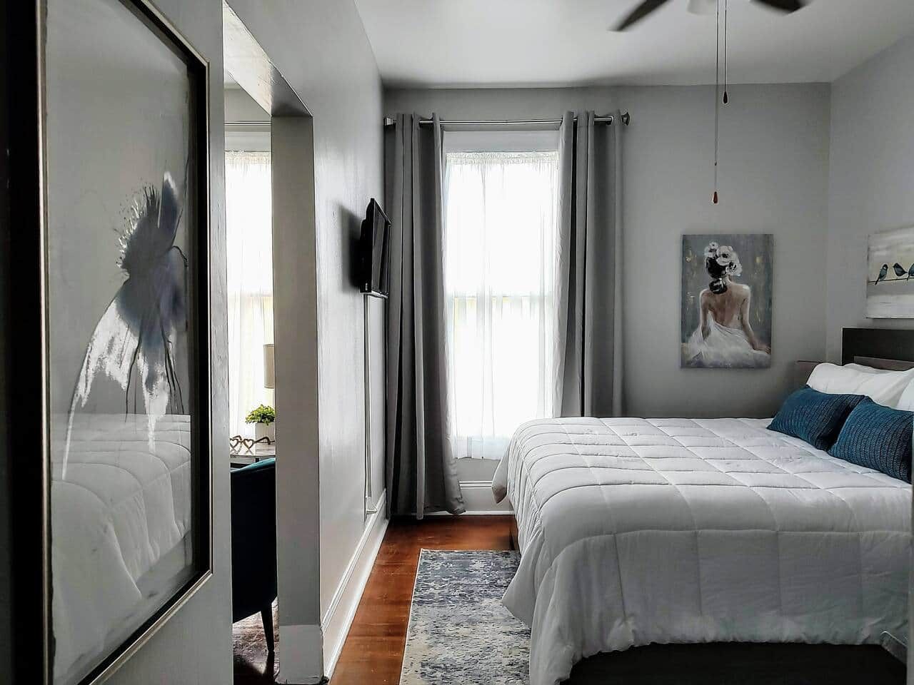 A modern bedroom with a large bed, a TV mounted on the wall, and a painting above the bed.