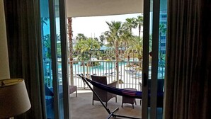A balcony with a hammock, a pool, palm trees, and a view of a building. - A Slice of Heaven - Destin! Pool View! (Destin)