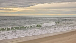 Une plage où les vagues se brisent près du rivage sous un ciel nuageux.
