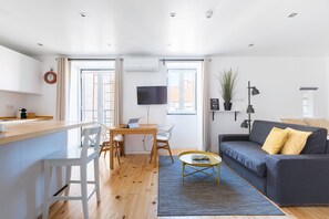 Un espacio habitable moderno con cocina, una mesa de comedor, un sofá y un televisor montado en la pared.