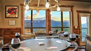 A round table with cards and wine glasses, set in a room with wooden walls and large windows overlooking mountains.