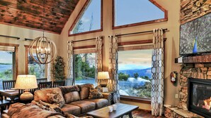 A spacious living room with a stone fireplace, leather sofas, and large windows offering a scenic view.