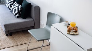 A modern living room with a grey sofa, a grey armchair, and a small white table with breakfast items.