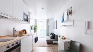 A modern kitchen with white cabinets, a wooden countertop, and a built-in oven. There is a dining area with a bench and a small table.