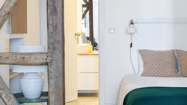 A bedroom with a bed, a bedside table, a lamp, and a wooden beam structure.