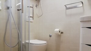 Ett badrum med en duschkabin med glasväggar, en toalett och en toalettpappershållare.
