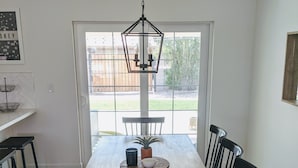 A dining area with a wooden table, black chairs, a hanging light fixture, and a view through a glass door to an outdoor space.