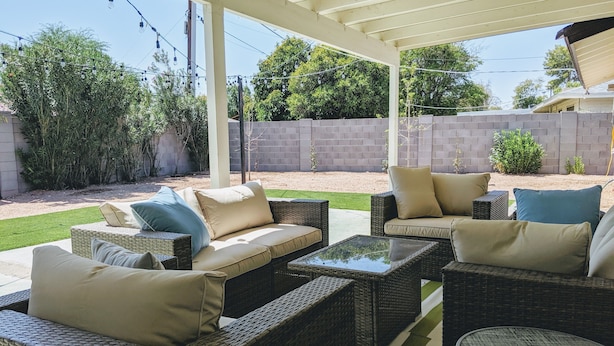 An outdoor patio area with wicker furniture, including sofas and a table, under a covered structure.