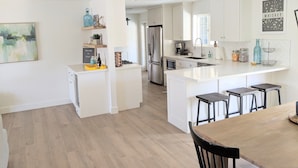 A modern kitchen with white cabinetry, a central island with bar stools, a built-in oven, and a refrigerator.