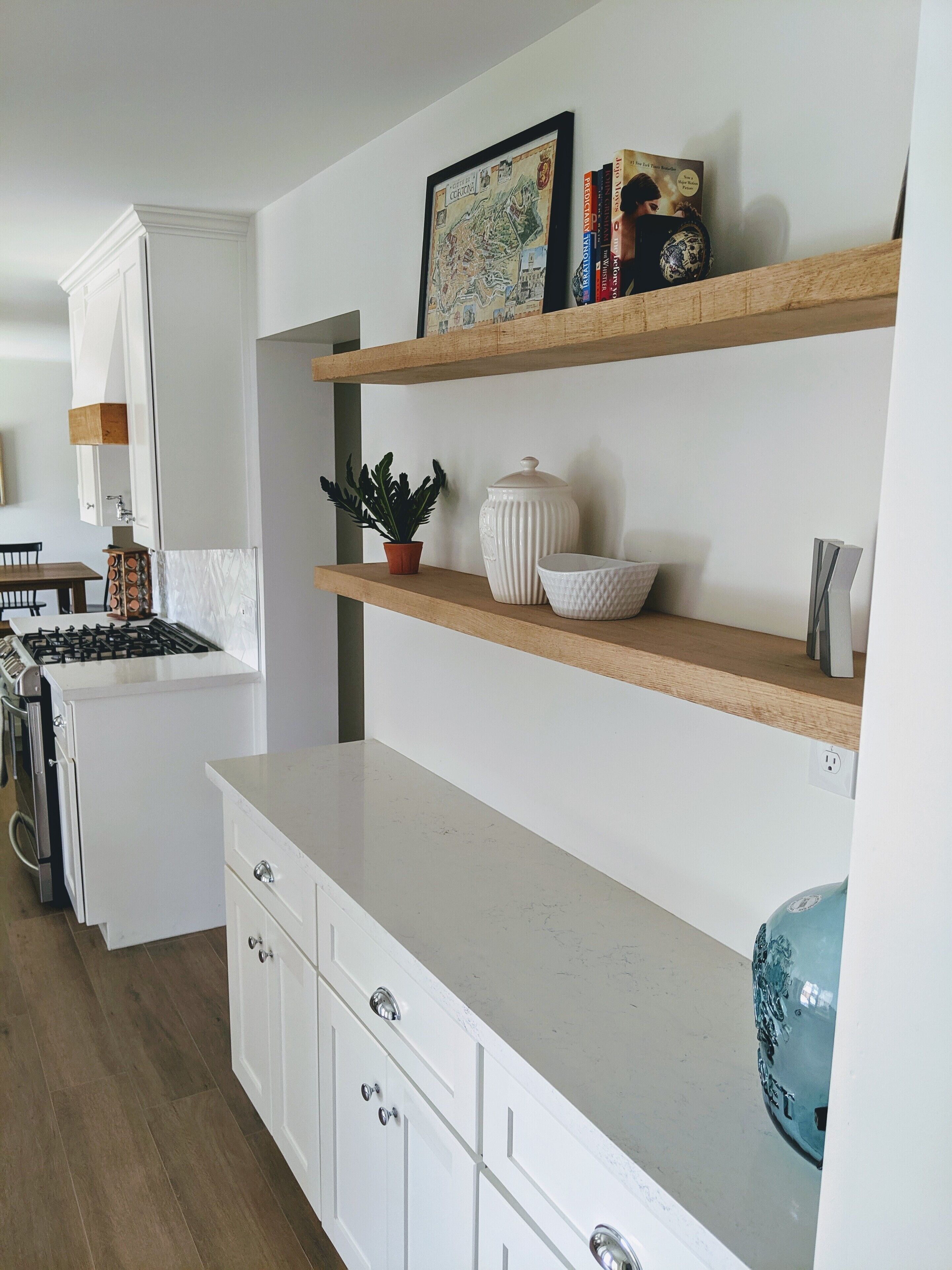 Una cocina moderna con armarios blancos, estantes de madera y encimera de mármol.