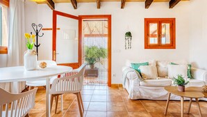 Una sala de estar con un sofá blanco, una mesa de comedor con sillas, una mesita redonda con una planta y un techo de madera.