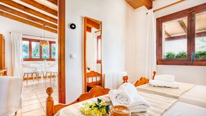 Habitación de hotel con techo de madera, cama con ropa blanca, una mesita con un florero y vista al jardín a través de una ventana.