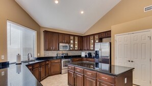 Una cocina con armarios de madera oscura, un refrigerador de acero inoxidable, un microondas y una isla grande con encimera negra.
