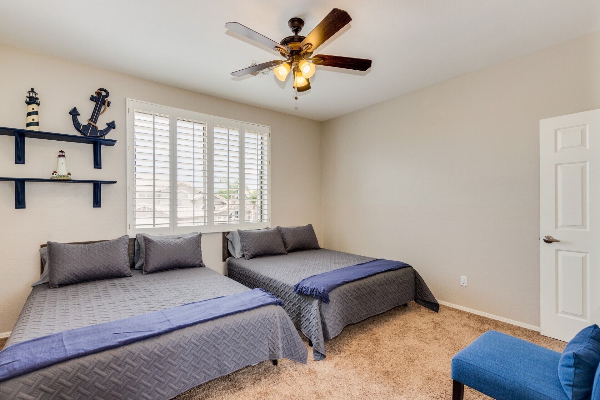 Quarto com duas camas, ventilador de teto e janela com cortinas.