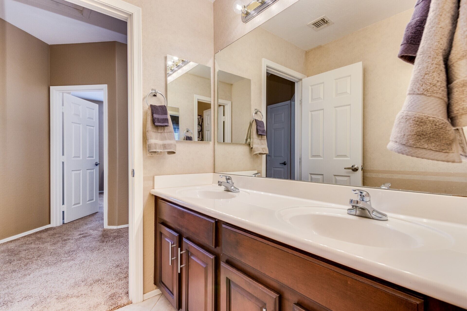 Une salle de bain avec deux lavabos, un grand miroir et une porte donnant sur une autre pièce.
