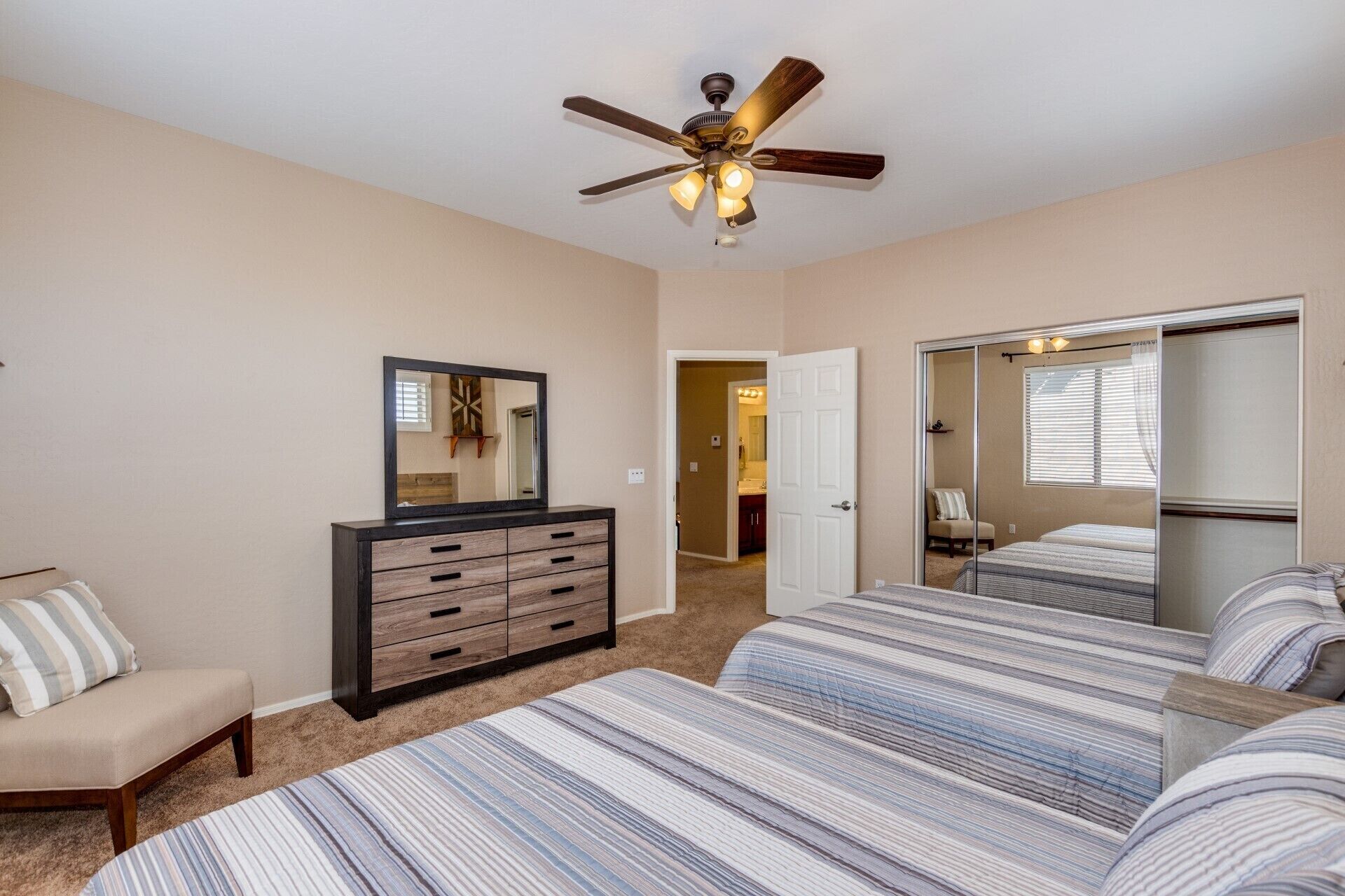 Quarto com cama, penteadeira, cadeira, ventilador de teto e espelho.