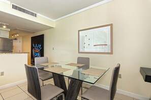 Un espace de salle à manger moderne avec une table et des chaises en verre, un tableau abstrait encadré et une cuisine en arrière-plan.