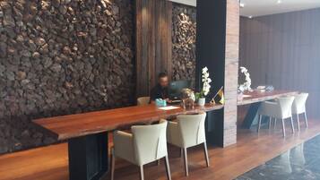 A reception area with a long wooden reception desk, several chairs, a stone wall, and a large screen.