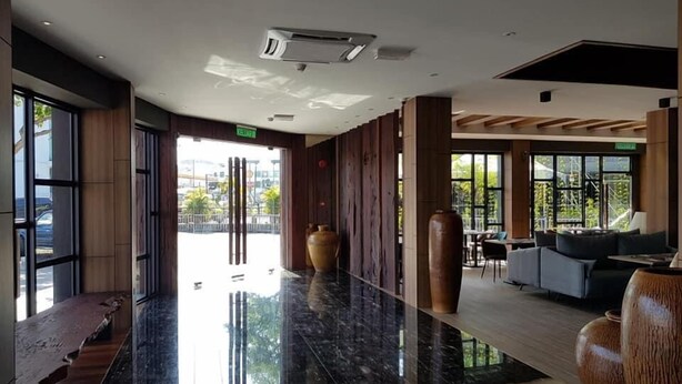 Un vestíbulo moderno con suelo de mármol, paneles de madera, ventanas amplias y una zona de estar con sofás y una mesa de centro.