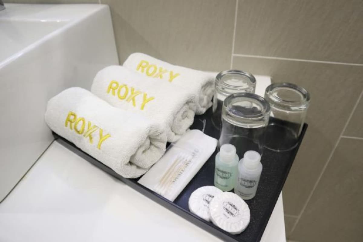Ett badrum med tre handdukar märkta med texten ”ROXY” och diverse toalettartiklar uppradade på ett bricka.