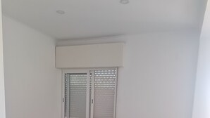 Una stanza piccola e arredata in modo essenziale, con un letto, un tavolino e una finestra con persiane.