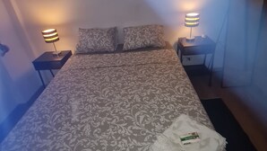 Un letto rifatto con cura, lenzuola decorate, due abat-jour e un asciugamano piegato sul letto.